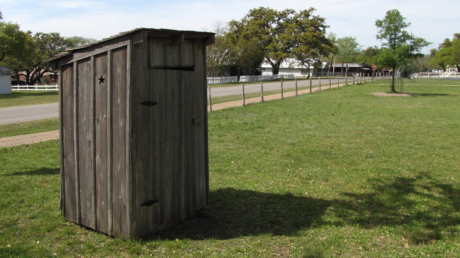 A small, wooden outhouse sits in the corner of the yard.