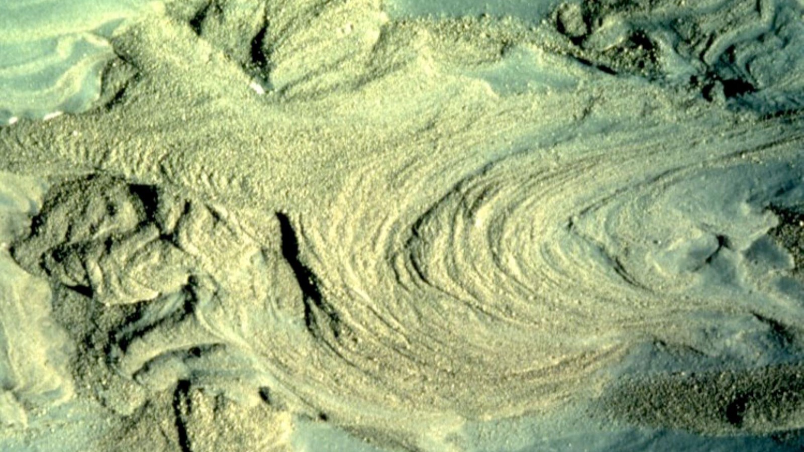 Large swirls of tan ash overlap on a blueish landscape. 