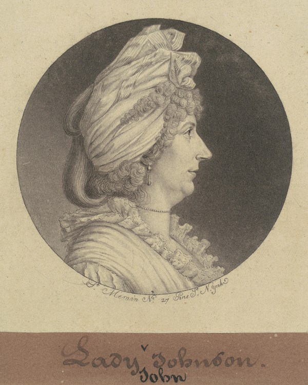A profile of woman with curls bundled up in a turban. Her gaze is focused.
