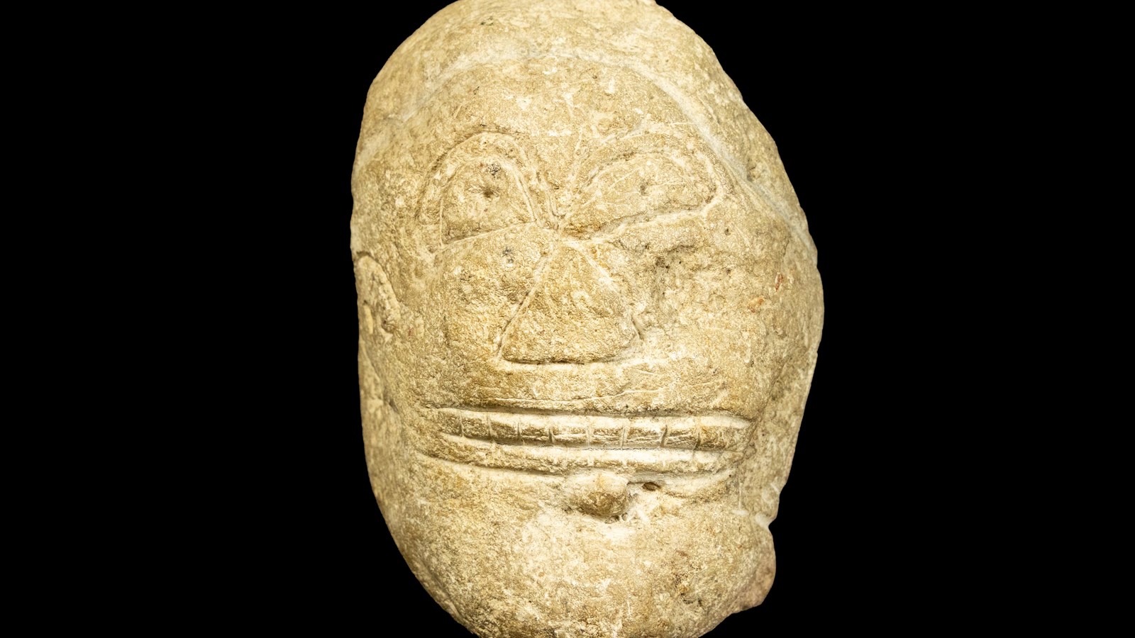 Carved stone Taíno zemí with stylized facial features displayed against a black background.