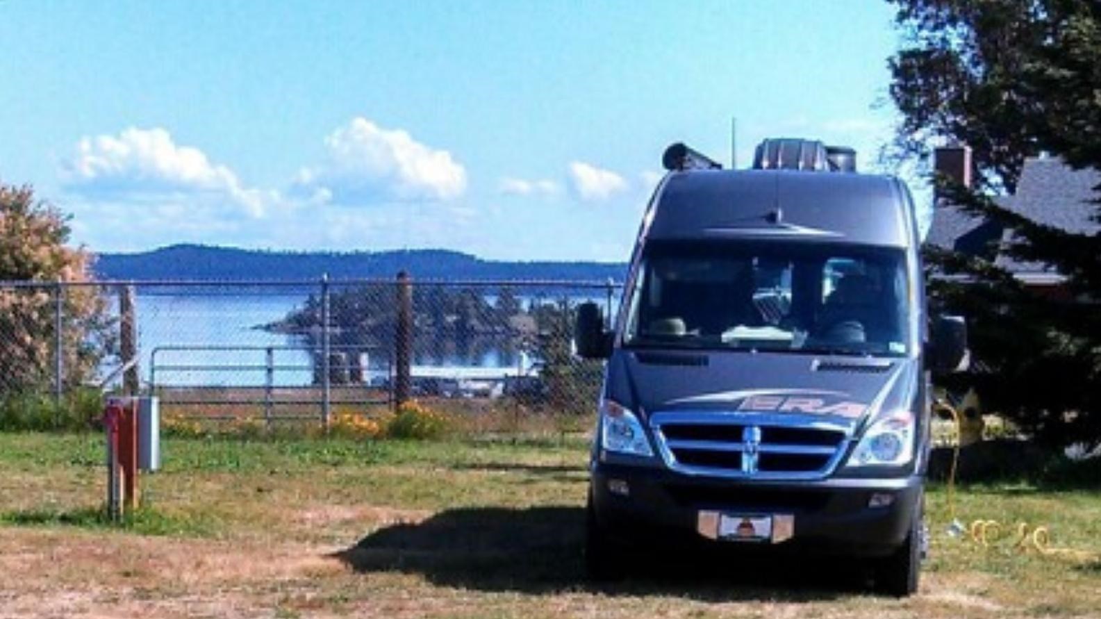 Color photograph of an RV in the grass in front of the ocean