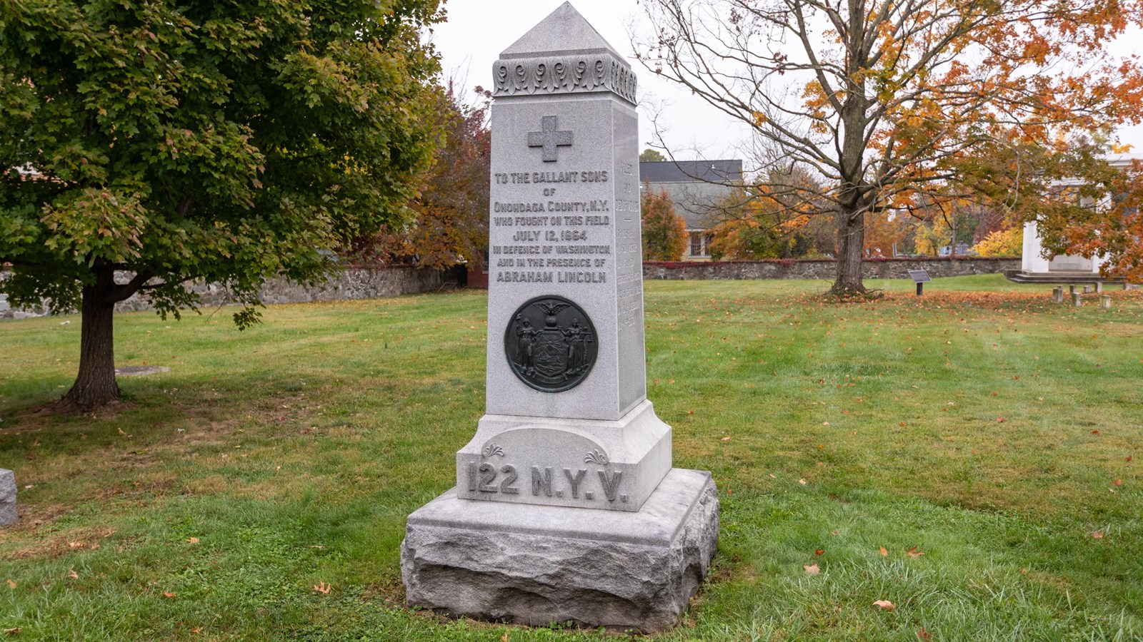 A stone monument stands in a cemetery on green grass on a cloudy day
