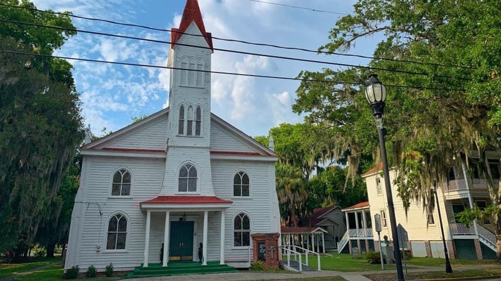 A two-story white church with a red roof and tall spire.