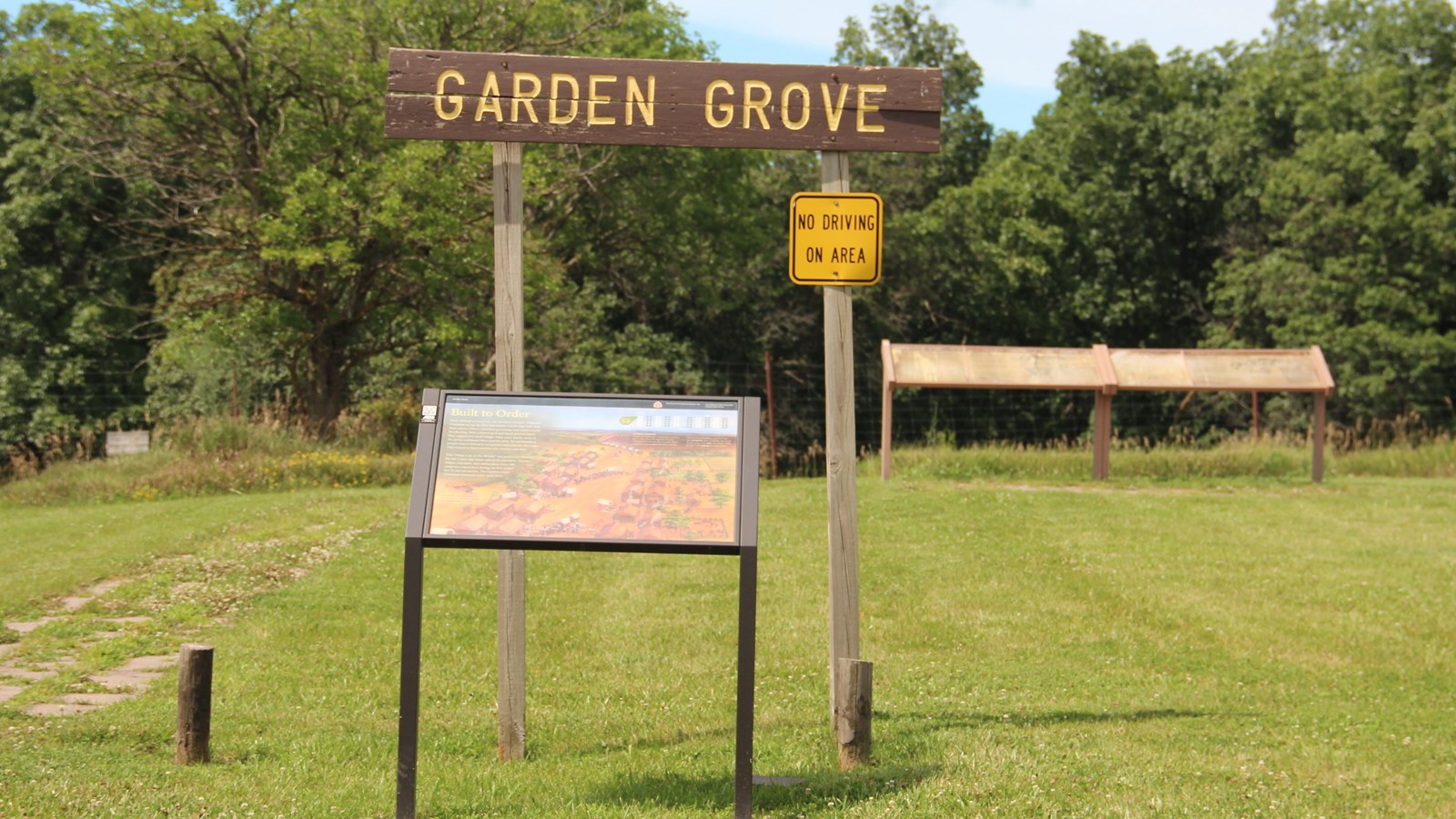 Center of grassy lawn is brown wooden sign with yellow words reading 