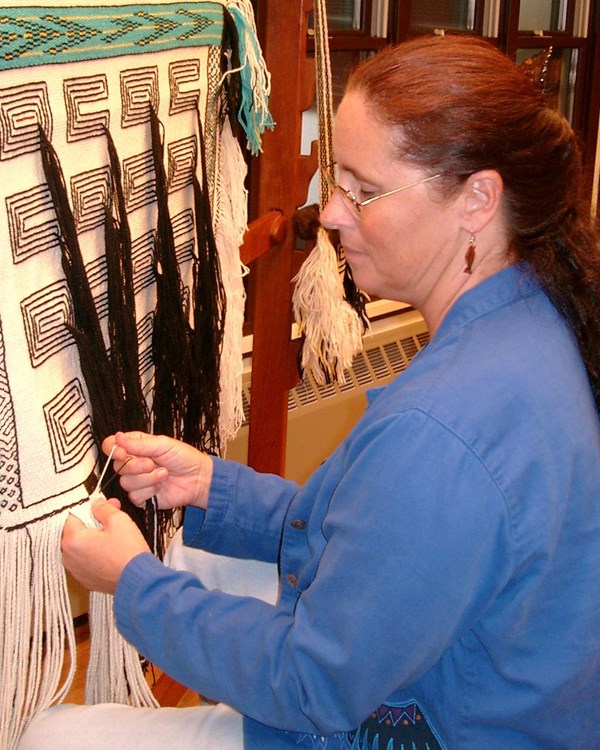 A woman demonstrates tradition weaving technique on a loom