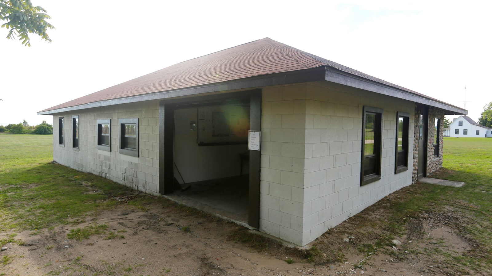 Square, hip-roofed, cinder-block building with garage door and many windows
