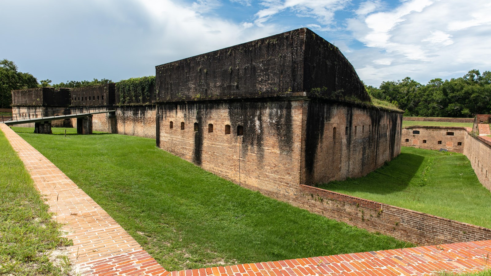 A large Civil War era fort with red brick walls and a drawbridge stands atop a grassy plain.