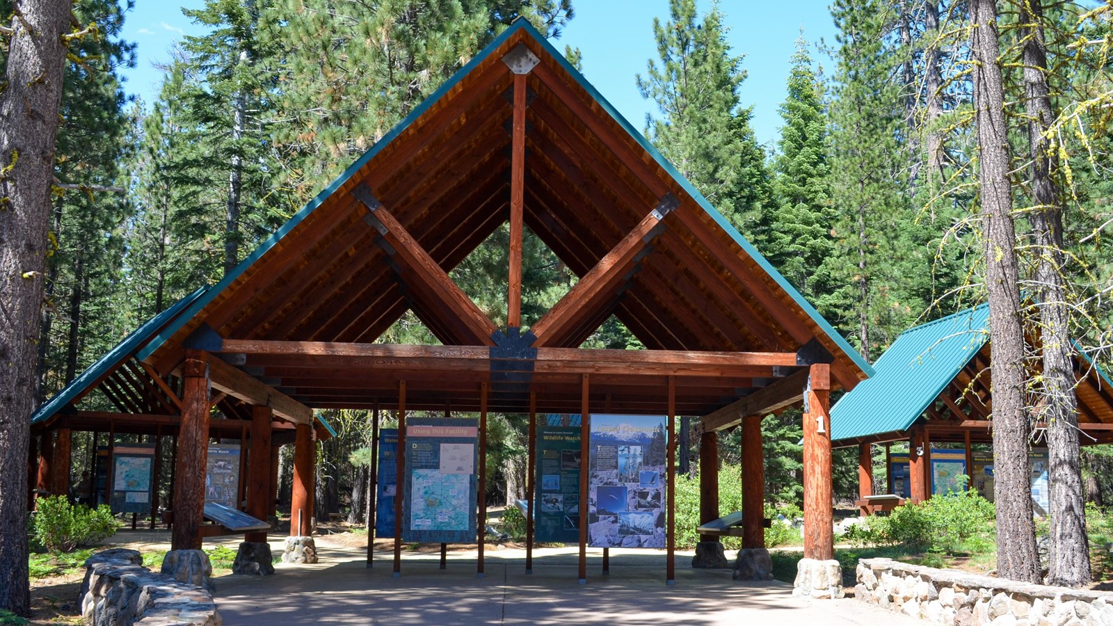 A color photo of three covered information pavilions amid conifer forests.