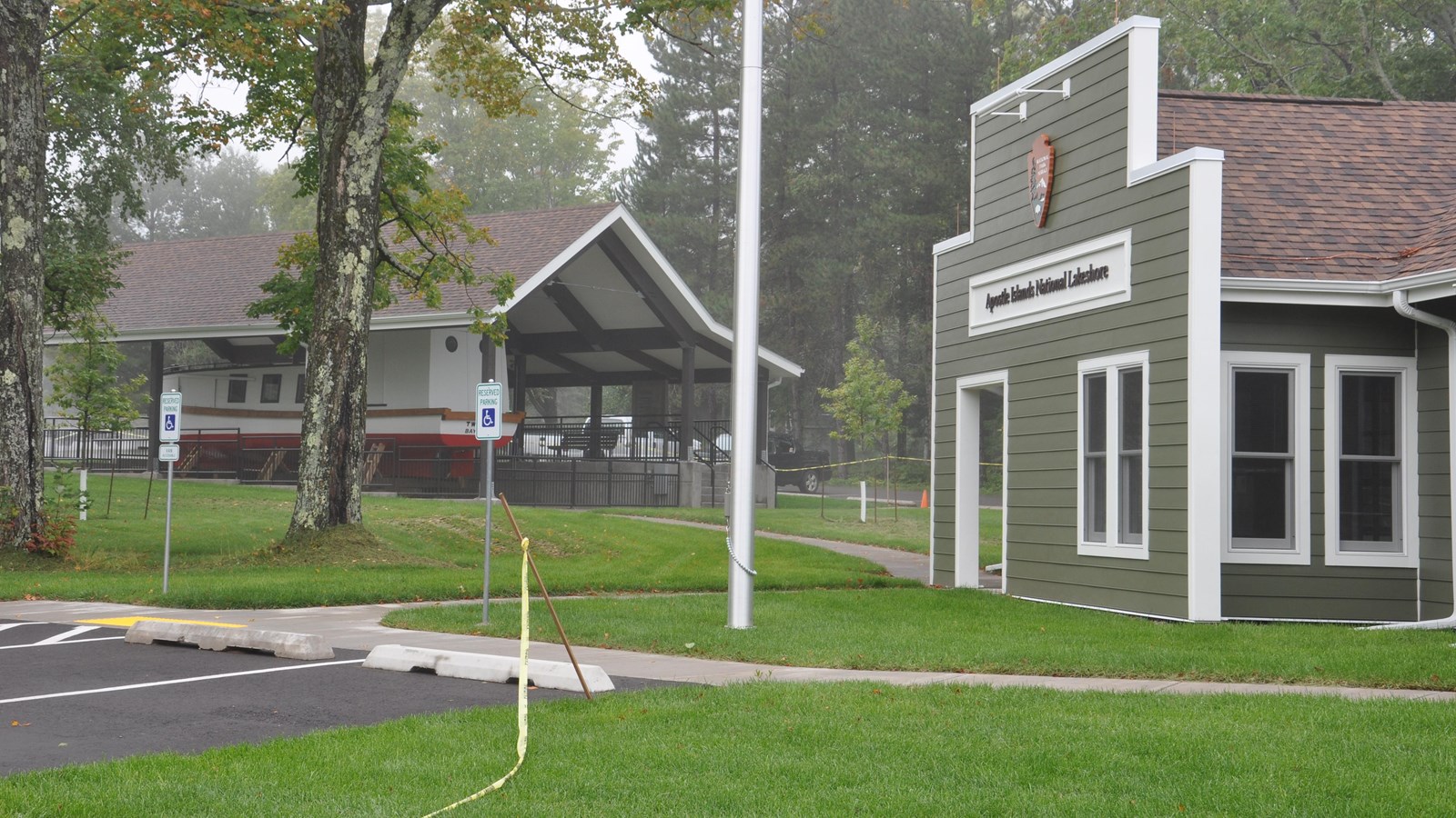 The side view of a green building with a brown roof and on a grassy lawn and a covered boat. 