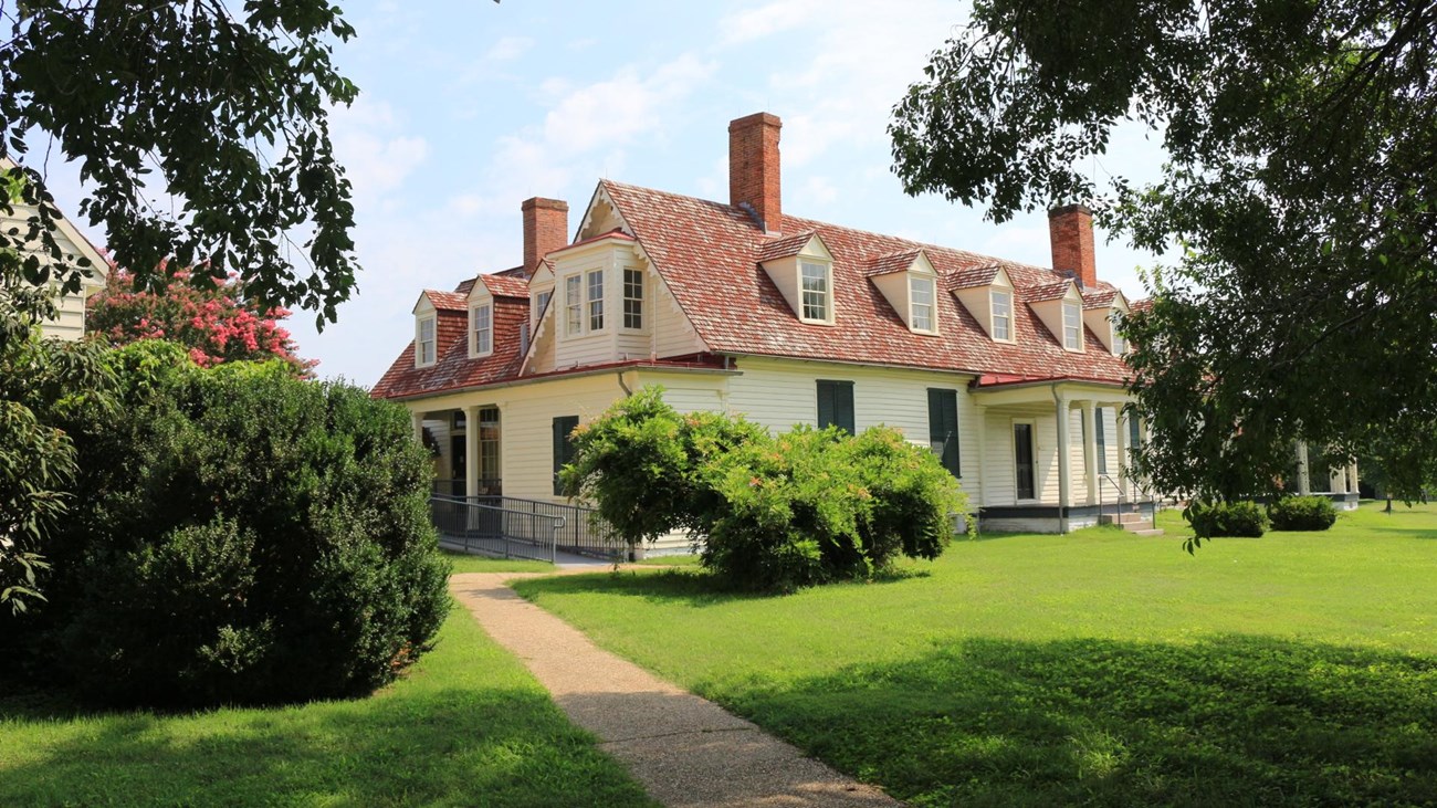 White two-story building with red roof and two red chimneys, tree in foreground of image.