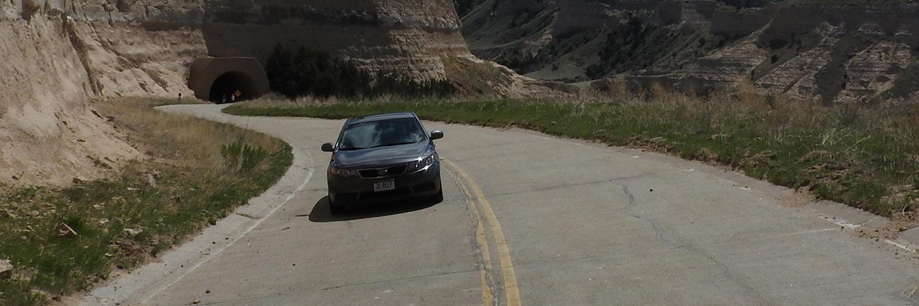 A car approaches a tunnel on a steep, winding road.