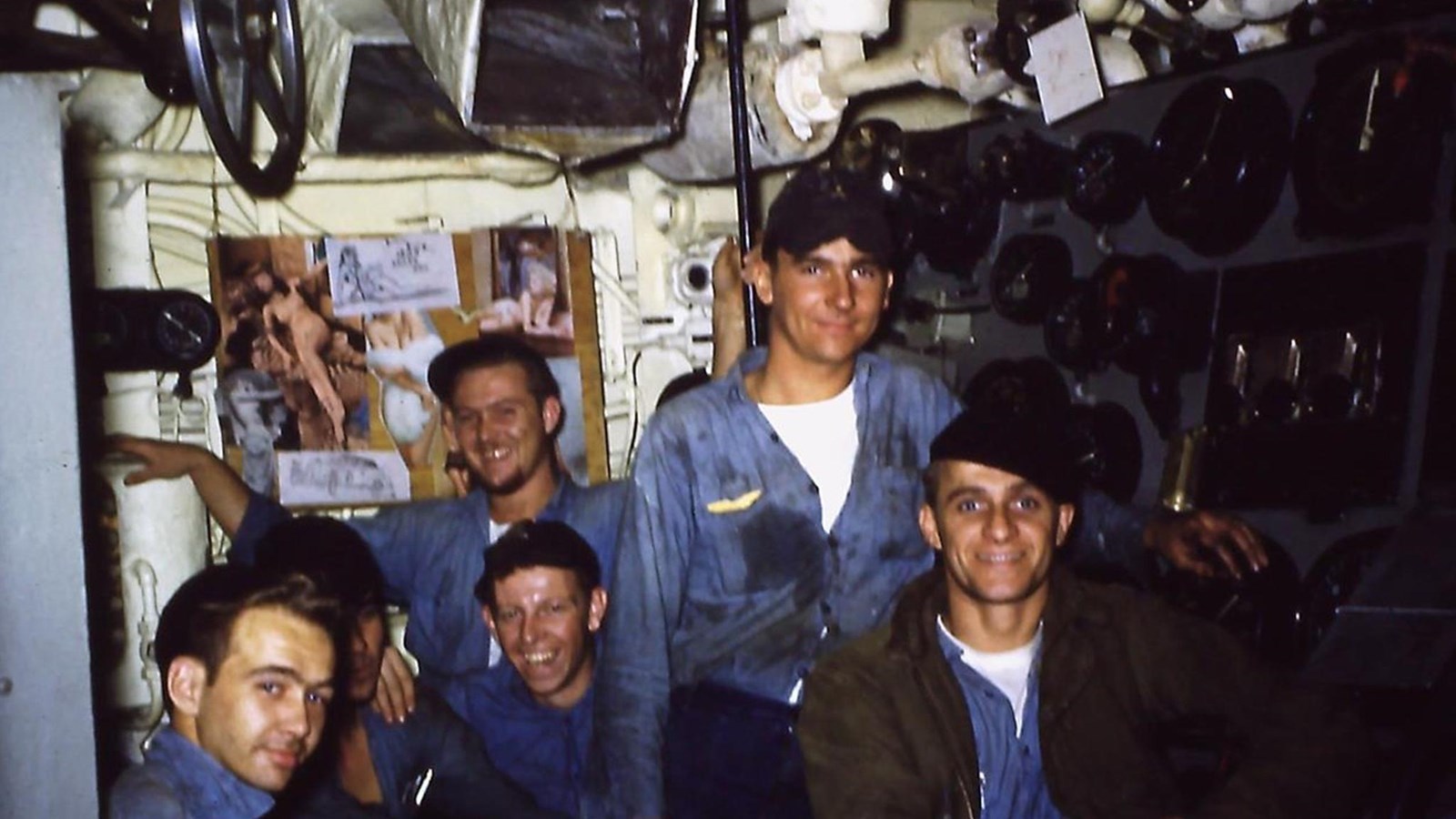 5 Crew members of a ship surrounded by valves and machines in the Engine Room. 