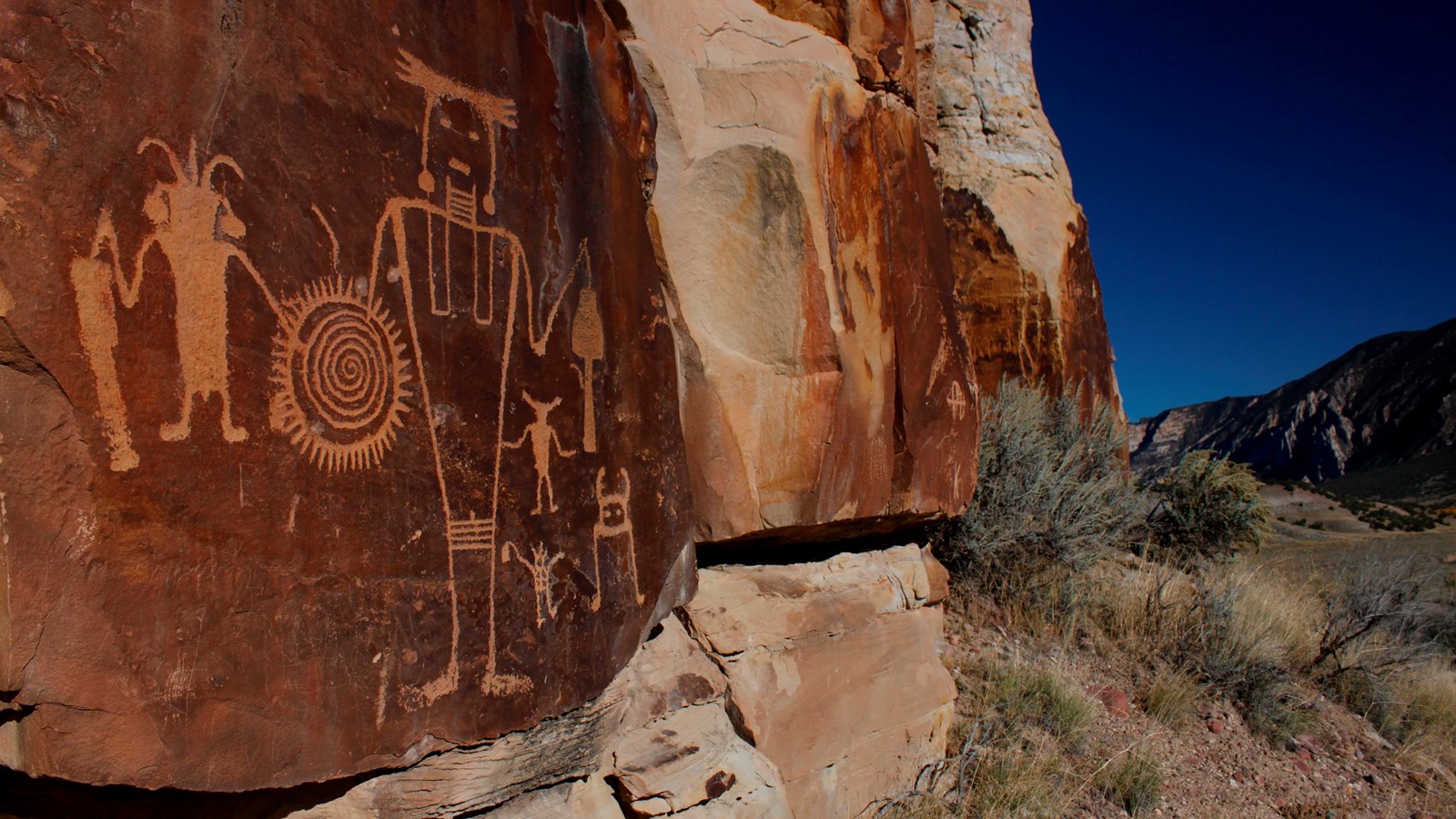 A variety of figures and designs are etched into the face of an orange-brown rock.
