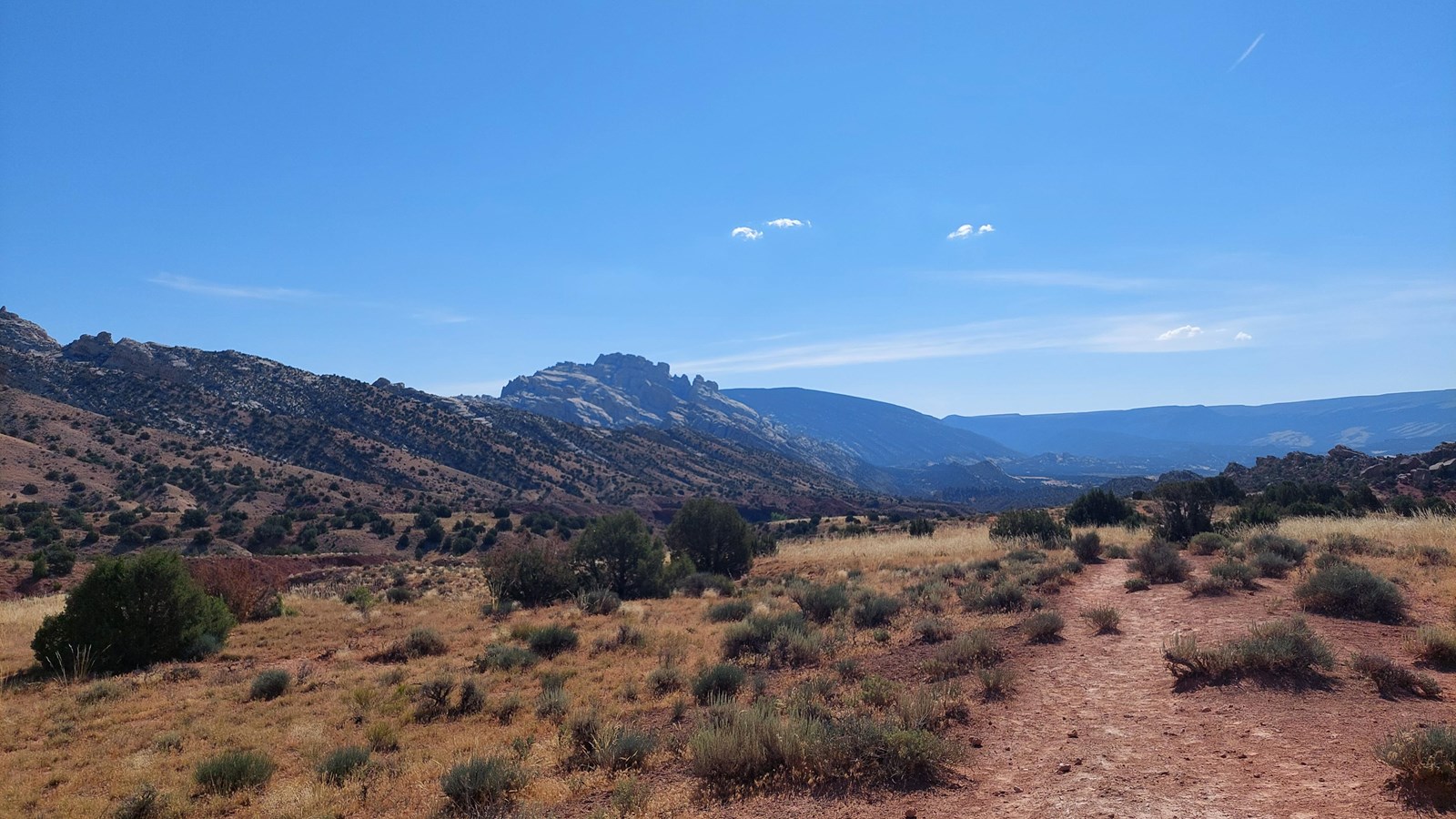 An open desert landscape with a view of a large craggy mountain in the distance beneath a blue sky.