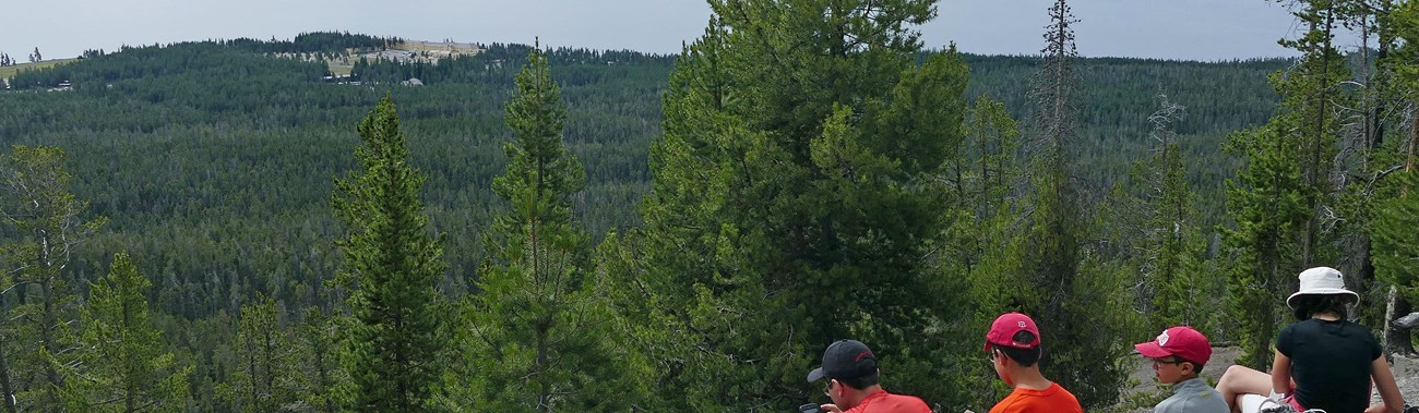 Hikers rest and look out at Yellowstone Lake from atop a mountaintop.