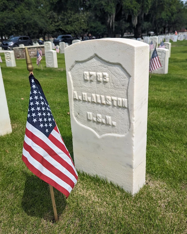 A small headstone that says AH Allston and has an American flag in front of it