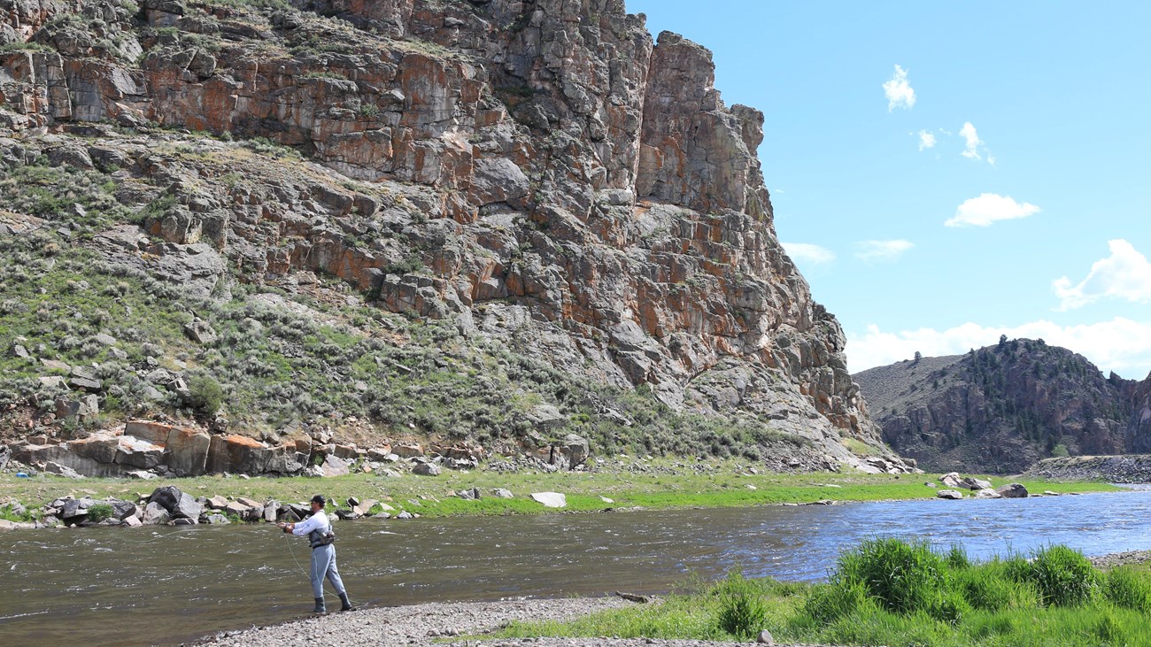 A person casting a fishing rod next to a river