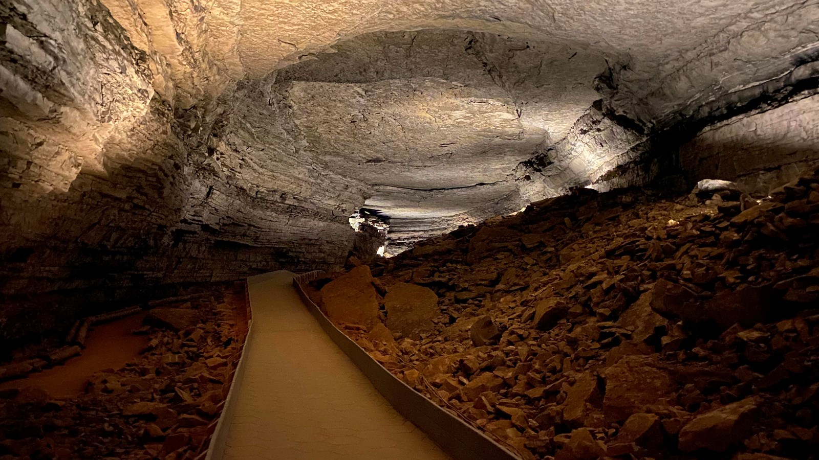 A large open cave passage with a paved trail down the center. A large pile of rocks is on the right.