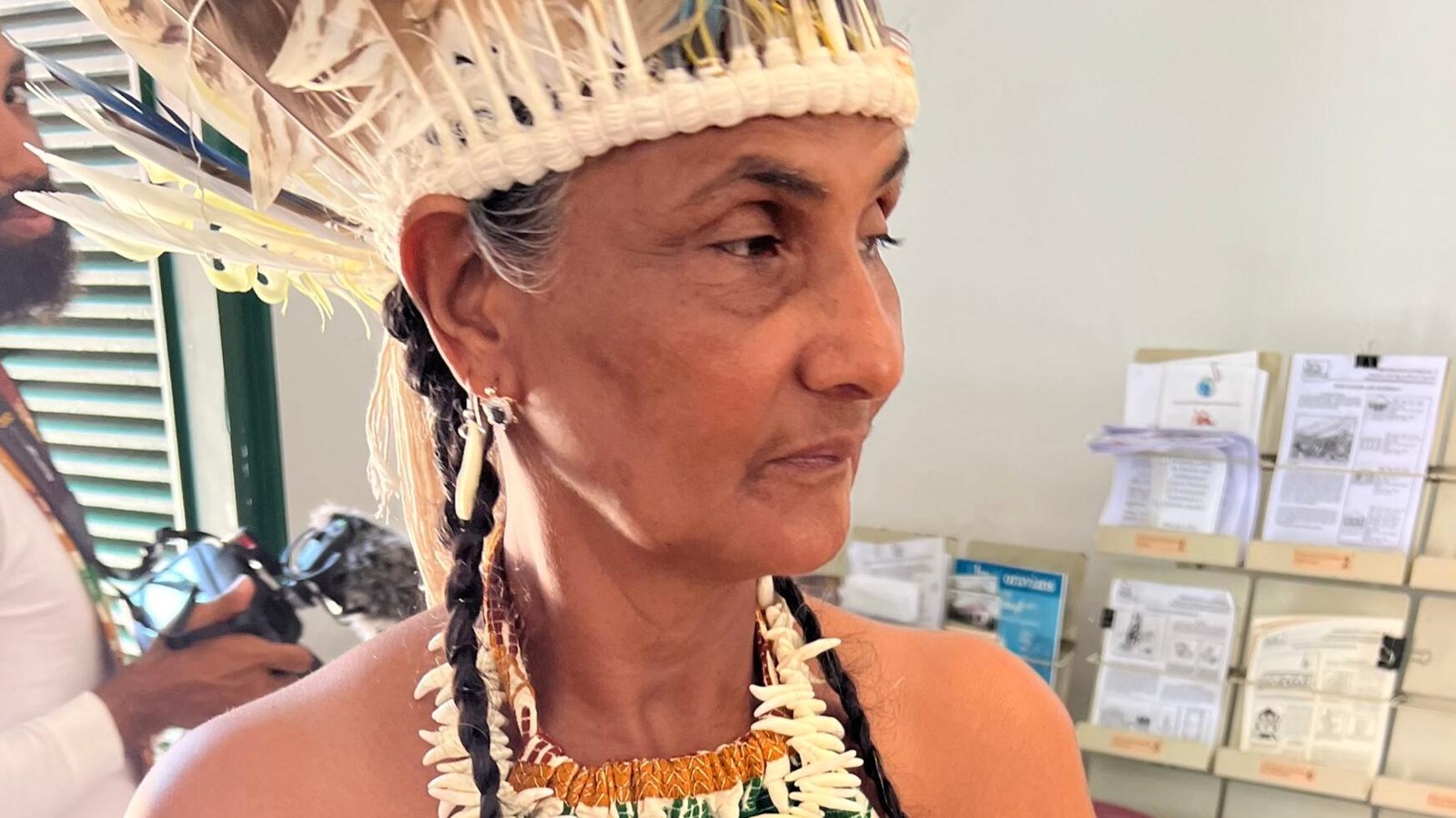 Woman in Taíno-inspired clothing and feathered headdress indoors.
