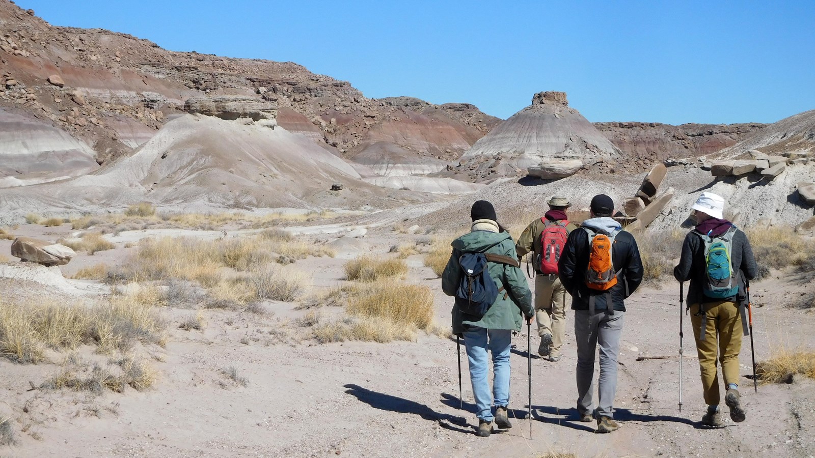 Hikers in the badlands and mesas under a blue sky.