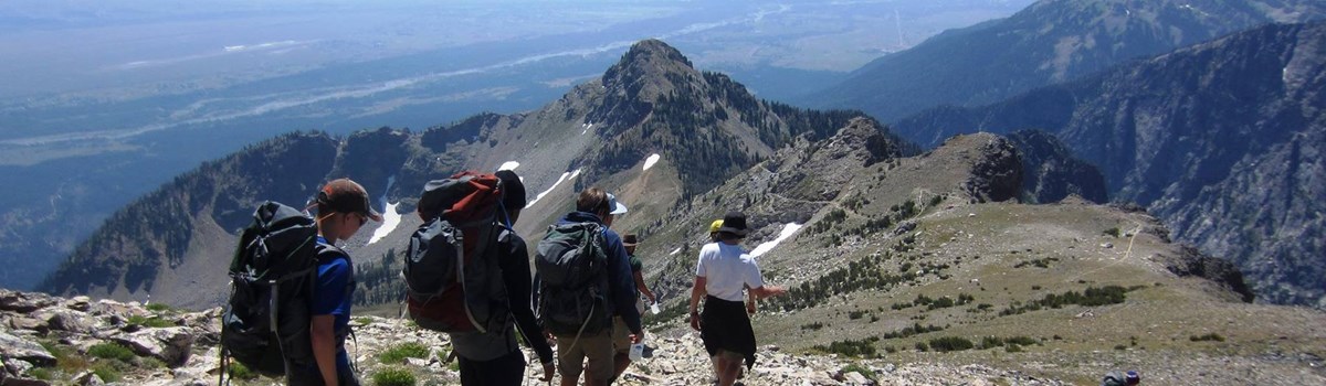 Four hikers walk down a steep, rocky trail.