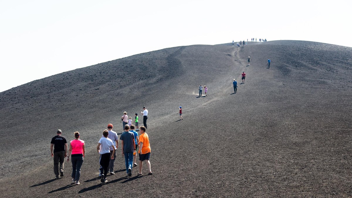 Visitors start a steep climb up a bare cinder slope.