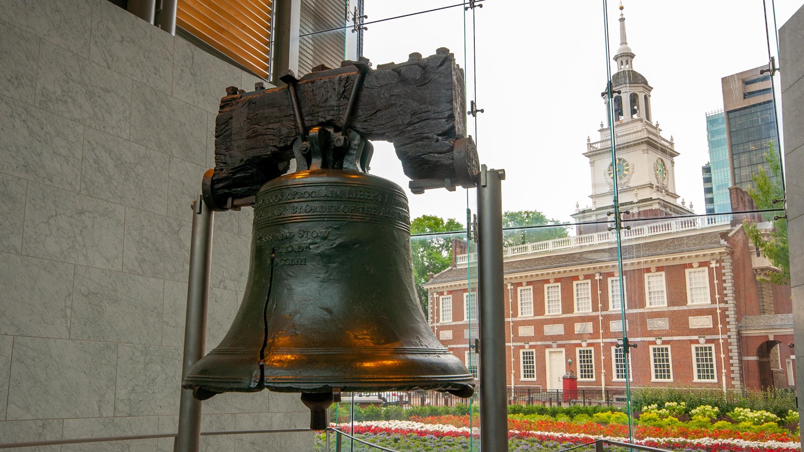 The Liberty Bell suspended on two posts, with Independence Hall in the background.