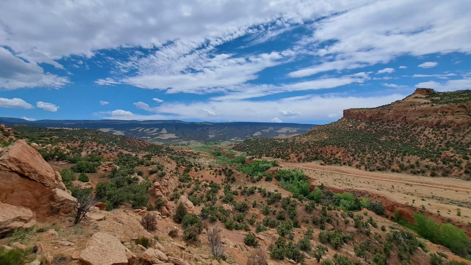 A narrow dirt road traversing a desert canyon heading towards a steep mountainside.