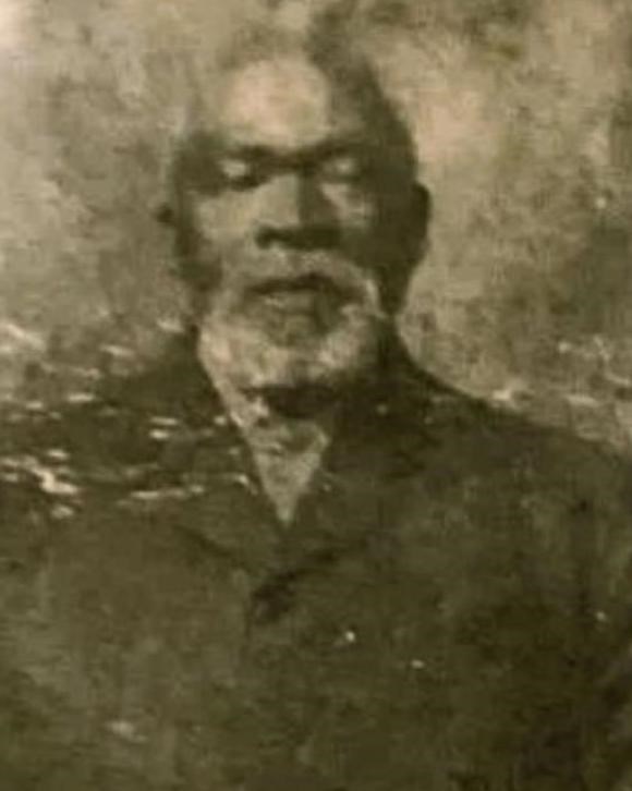 Faded B&W photo of black man with gray gotee and a black button overcoat.