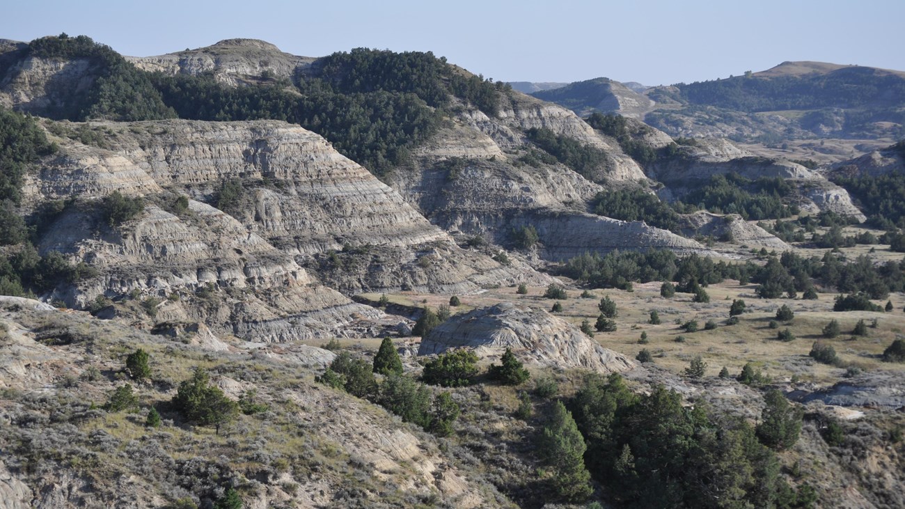 The badlands, including a view down into a sandy bottomed valley and large buttes under a cloudy sky
