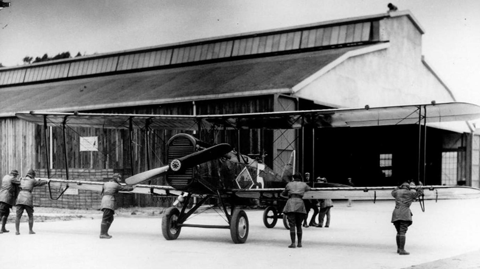 Pilots push a biplane to a hangar in the 1920s. 