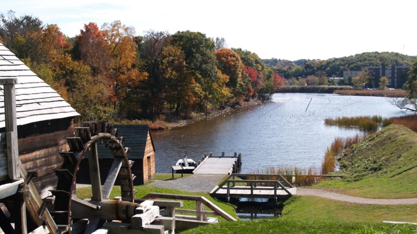 paved path leads to a small wooden warehouse and dock on a river