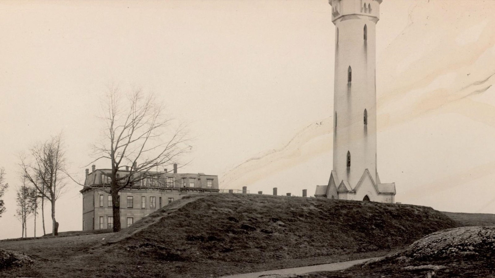 Black and white historic photograph of hill, tower, and buildings in background.