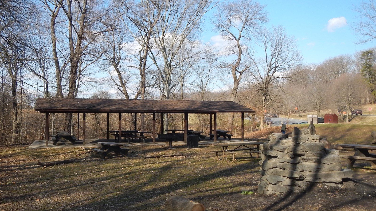 A picnic pavilion, stone grill and grassy area surrounded by trees. 