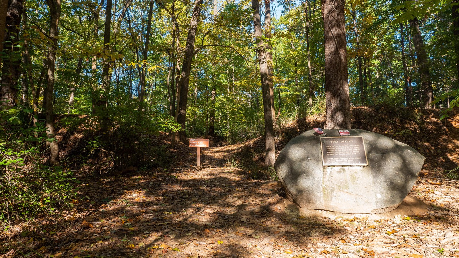 The Fort DeRussy earthworks, with a keep off sign and a large boulder with a plaque noting the impor