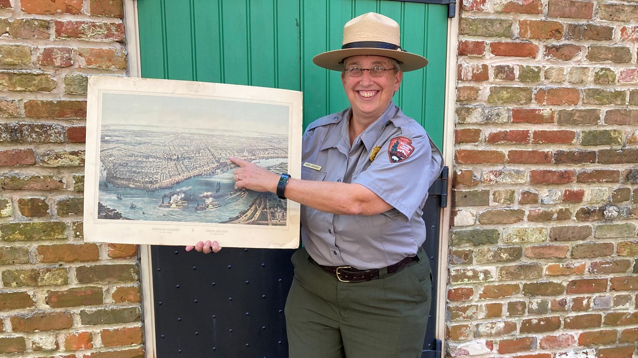 Ranger Karen in a flat hat holding a historic painting of new orleans