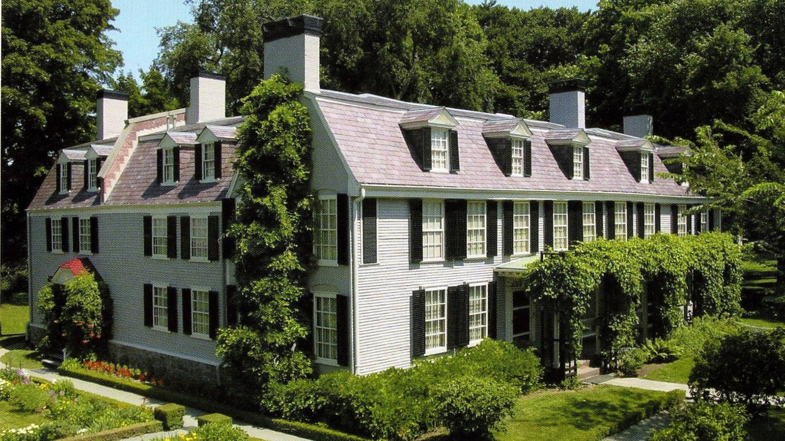 A grey, two story building.  View from the front corner.  Green wisteria and vines.