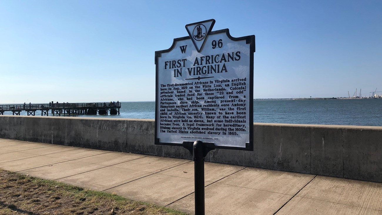 A historical marker sign on a seawall notes the arrival of the first Africans in Virginia.