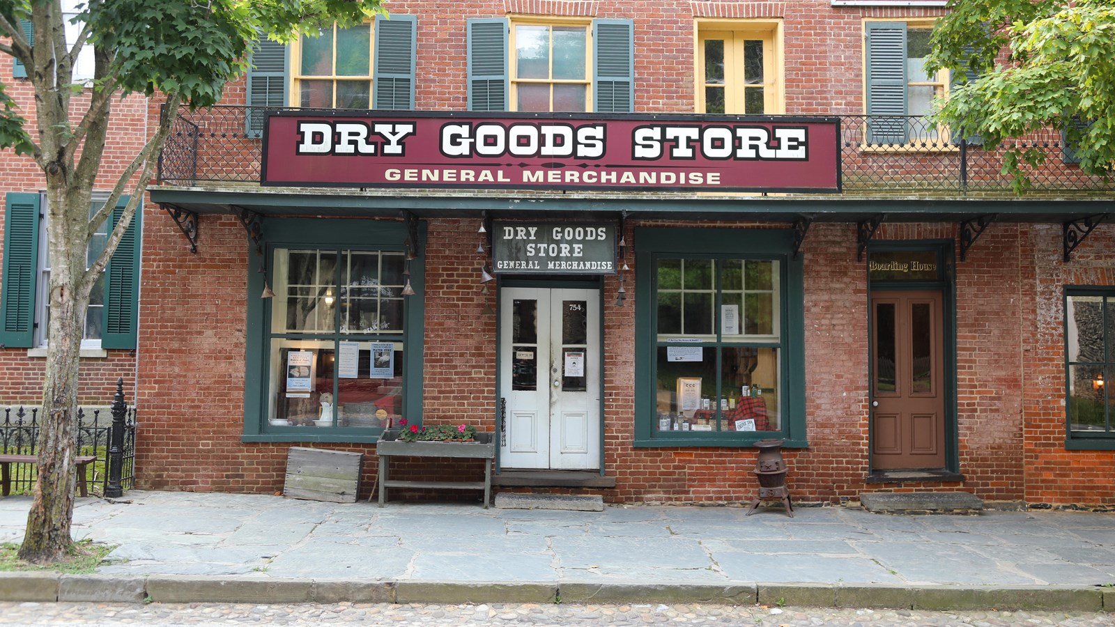 Brick storefront with front door set between two windows below large sign reading: Dry Goods Store.