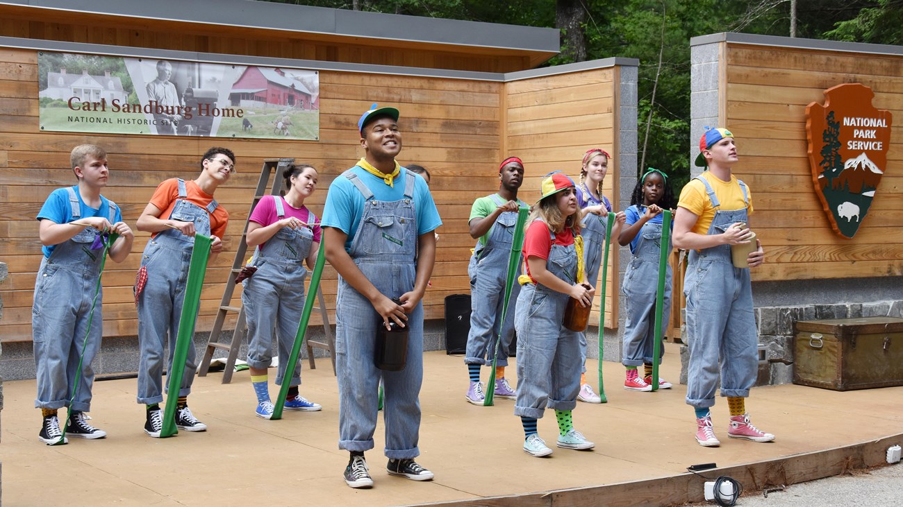 several actors are on stage wearing overalls and colorful shirts