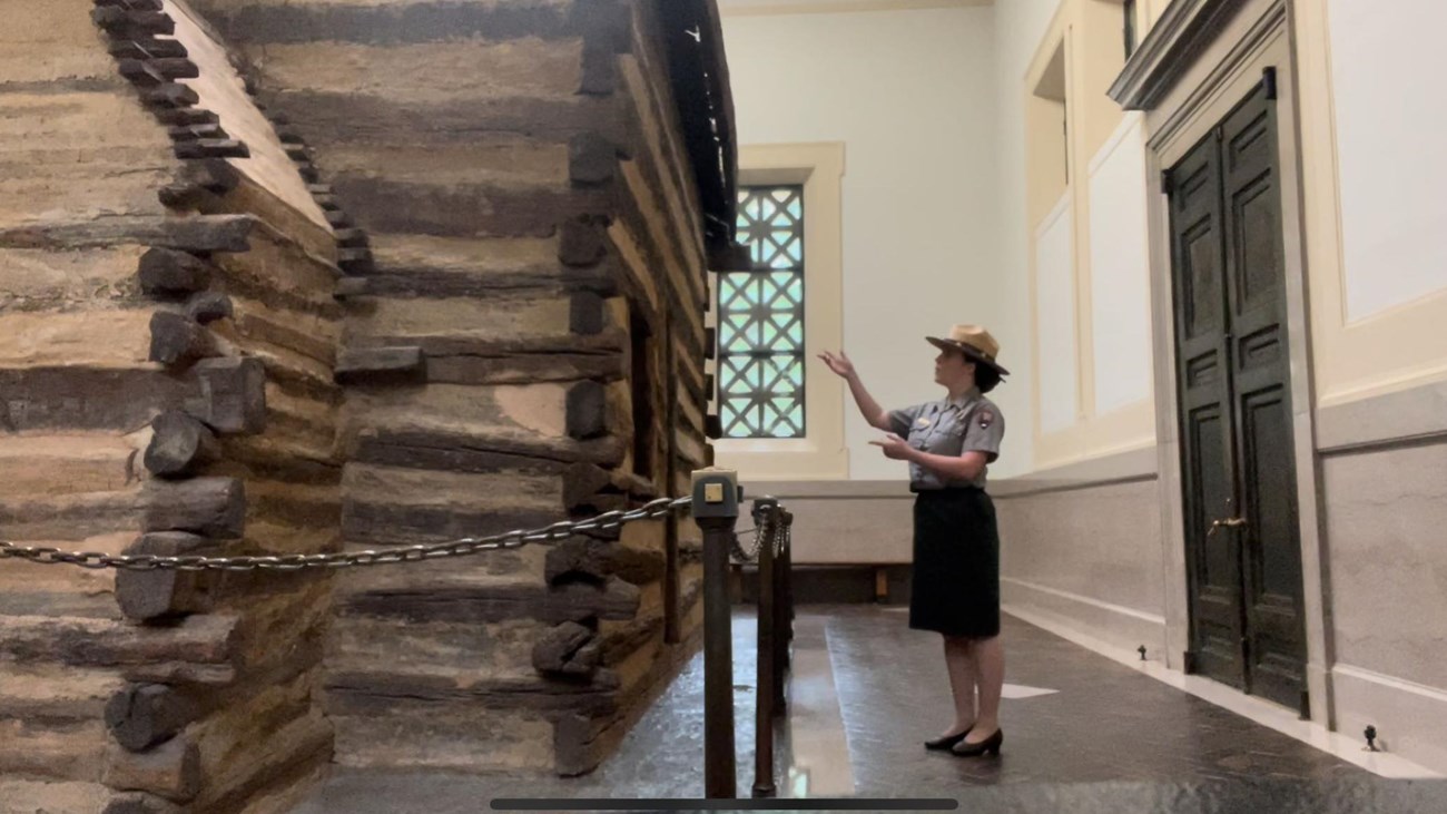 Ranger pointing at single room log cabin