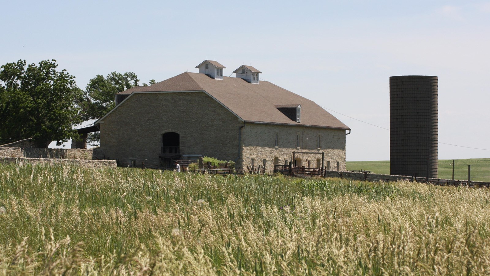 A three story stone barn stands beyond the grass field.