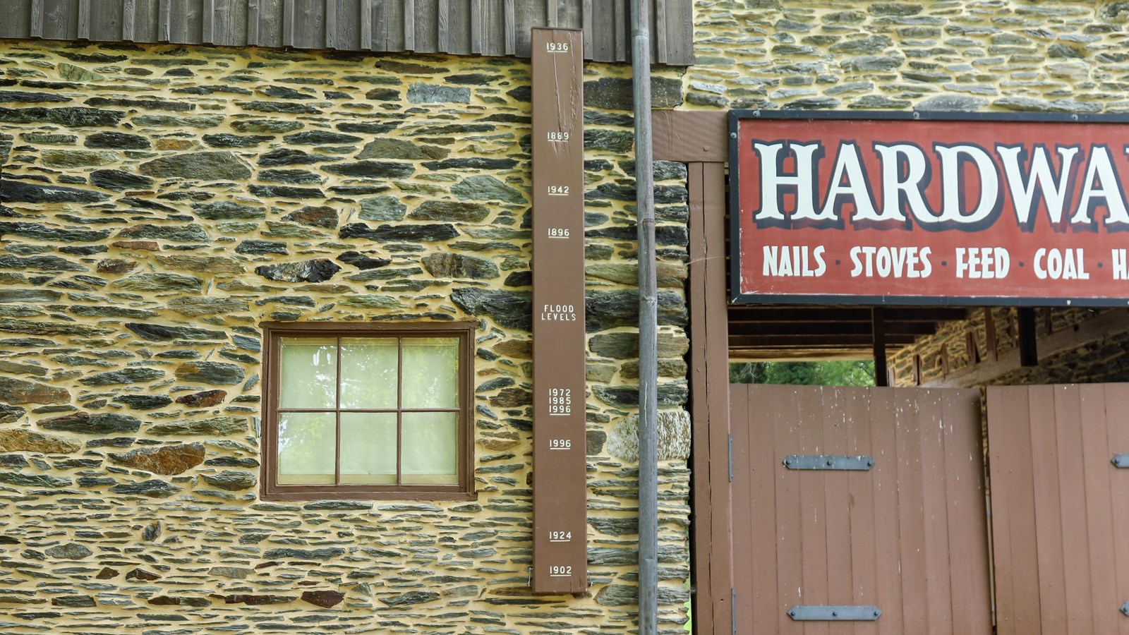 A brown plank fixed to the wall of a building, painted to show water levels of past floods.