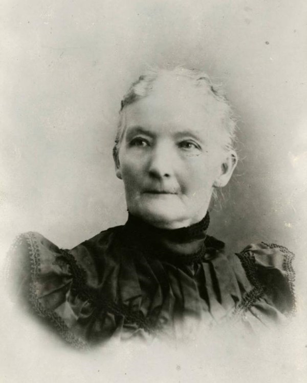 A black and white portrait of a woman with white hair pulled back in a dark colored period dress