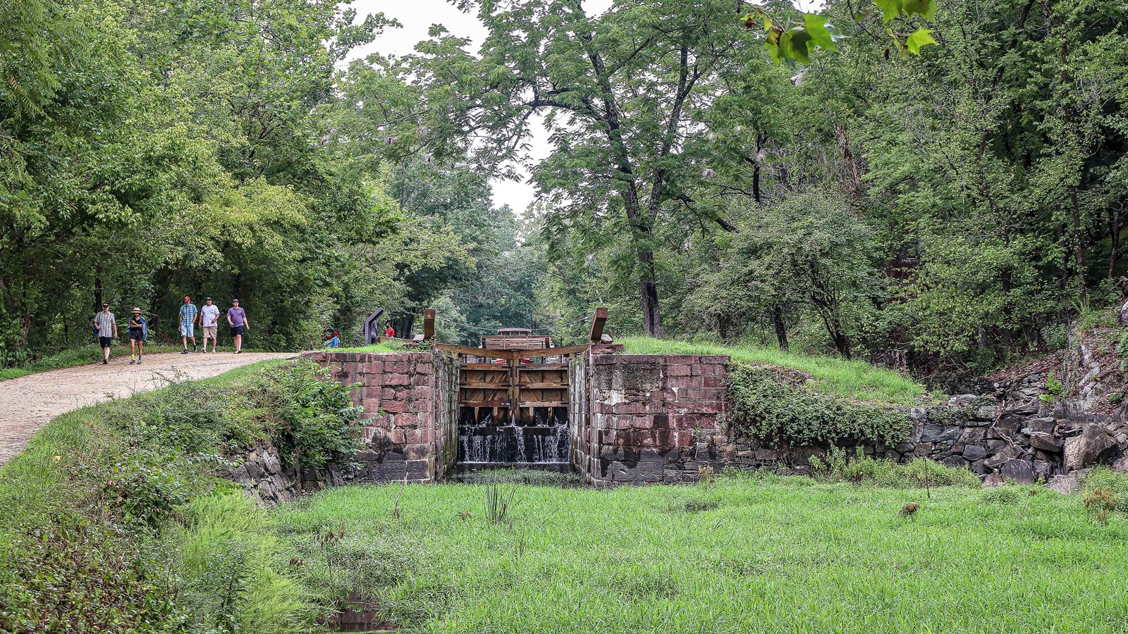 People walk along the towpath next to a stone made lock.