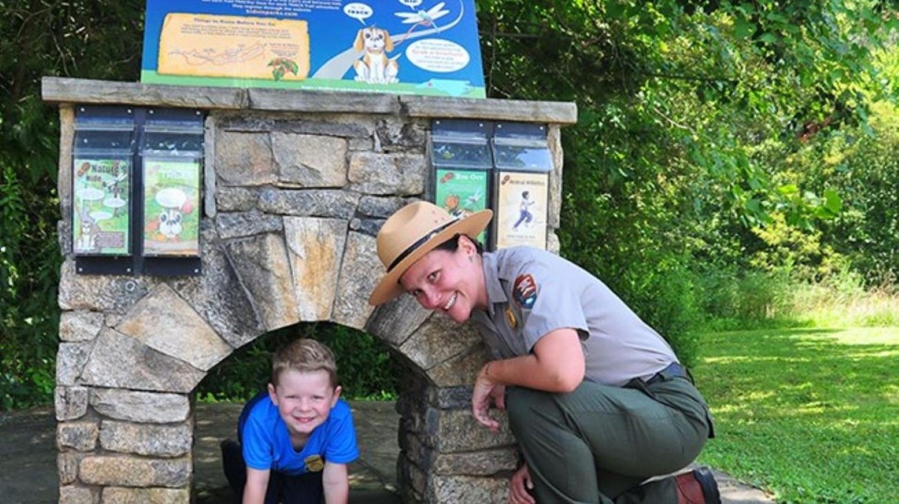 Park ranger and young boy pose in front of a small stone arch and information sign