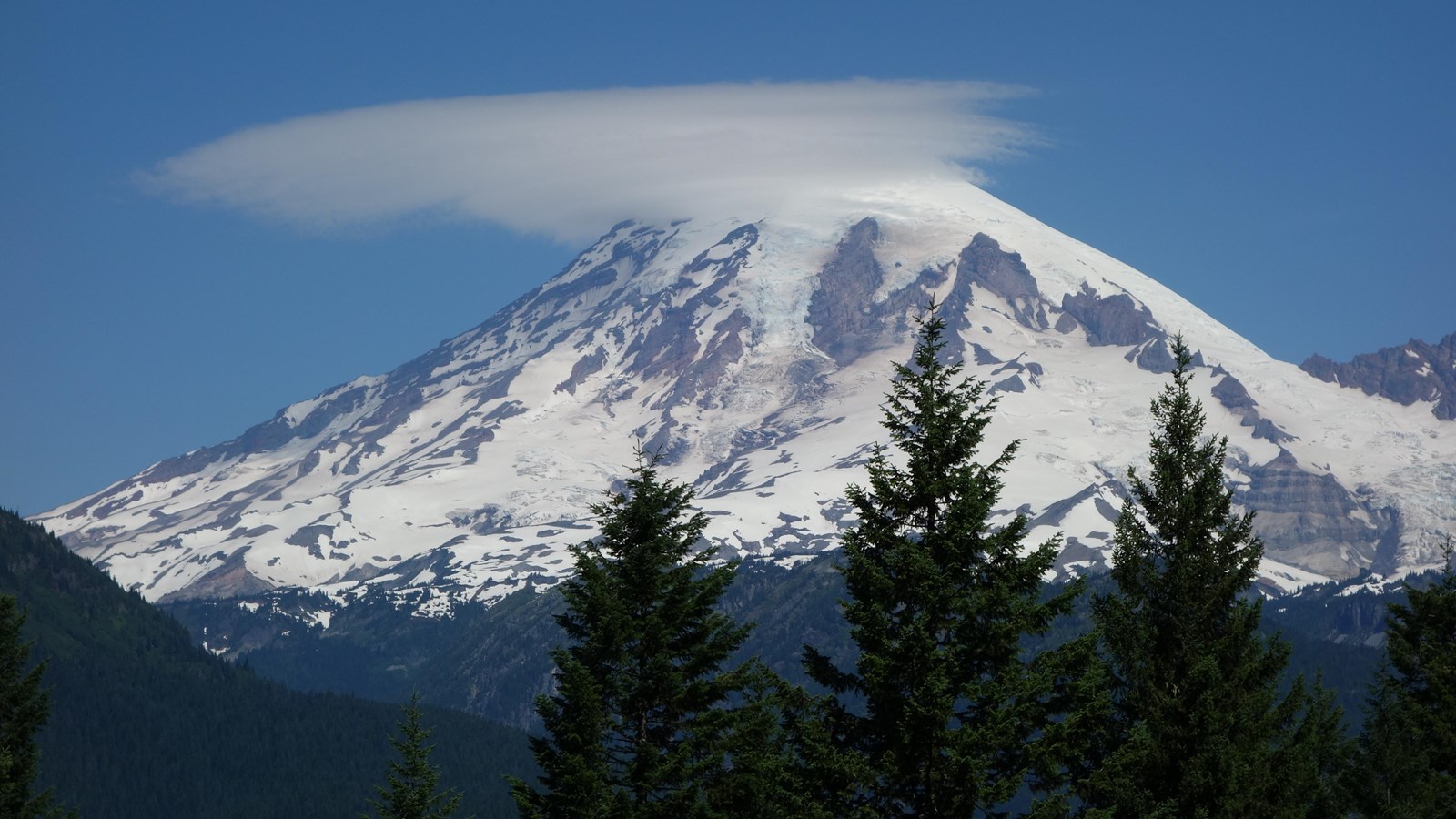 A glaciated mountain with lenticular clouds streaming from the peak.