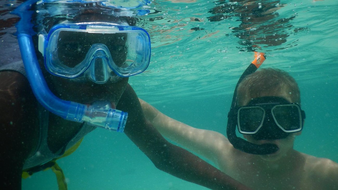 Two young swimmers wear mask and snorkel in clear water.