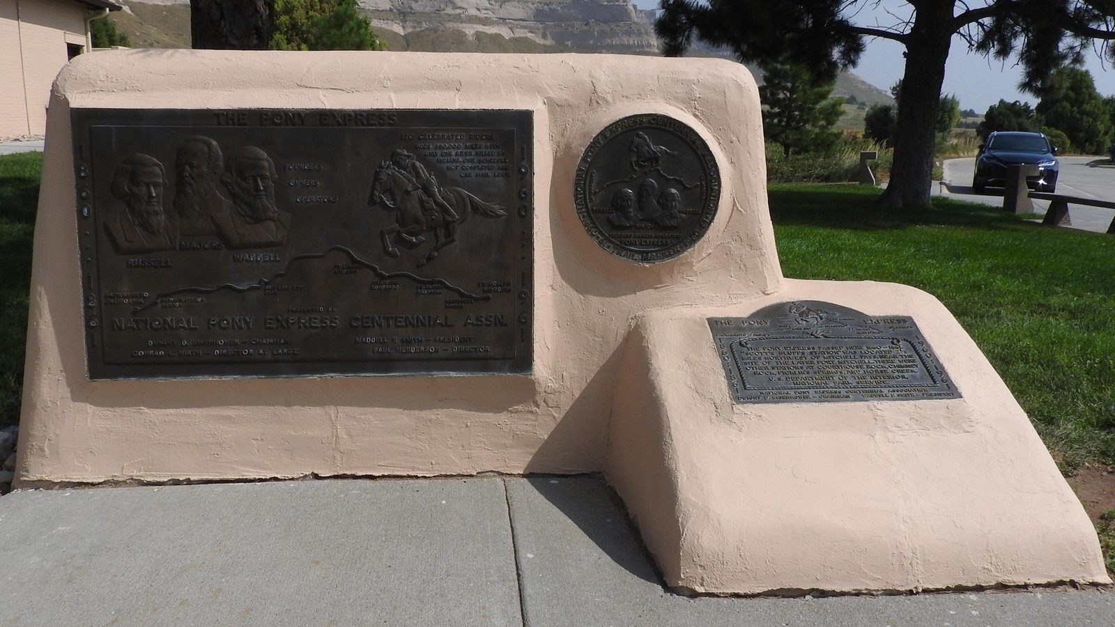 A concrete monument with stucco covering and three inset metal engravings. 