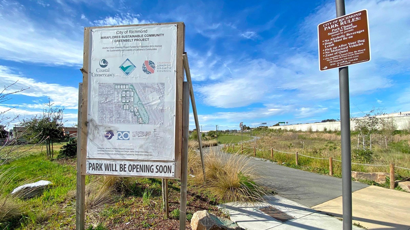 A temporary sign sits next to a park entrance trail. 